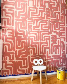 a white chair sitting in front of a wall with red and pink designs on it