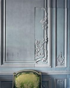 a green chair sitting in front of a gray wall with ornate carvings on the walls