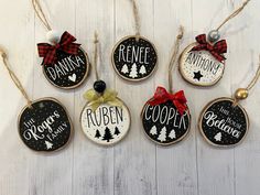 christmas ornaments hanging from strings on a white wooden surface with pine trees and words painted on them