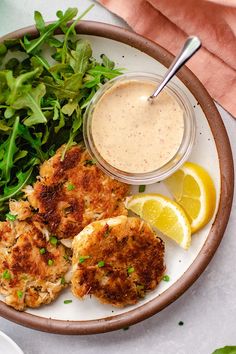 a white plate topped with crab cakes next to a salad and dipping sauce on top of it