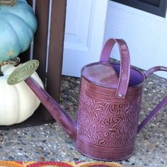 a purple watering can sitting on the ground next to a white pumpkin and other fall decorations