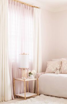 a white bed sitting in a bedroom next to a window with sheer curtains on it