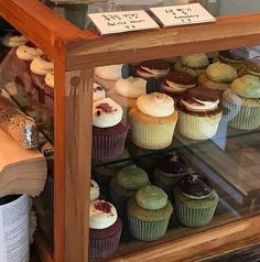 a display case filled with lots of different types of cupcakes on top of wooden shelves