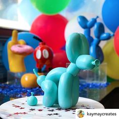 a blue balloon dog sitting on top of a white plate next to balloons and confetti