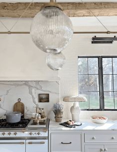 a kitchen with white cabinets and marble counter tops, hanging lights over the stove top