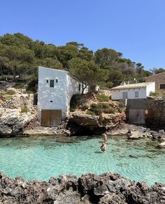 people are swimming in the clear blue water near some small buildings and trees on top of a hill