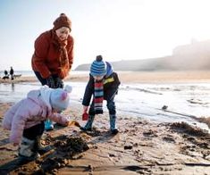 two children playing on the beach with an adult and one child in winter clothing looking at something