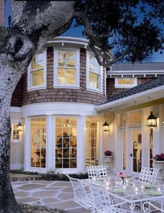 an outdoor dining table and chairs in front of a large white house with lots of windows