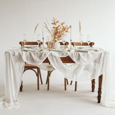 the table is set with white linens and place settings for four people to sit at