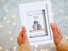 a person holding up a white frame with two rocks in it and the words stones wedding anniversary