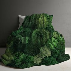 a blanket with green plants on it sitting on top of a white table next to a pillow