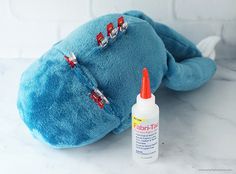 a blue stuffed animal with red pins on it's back and a bottle of glue next to it