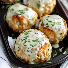 three meatballs covered in cheese and parsley on a black plate with napkins