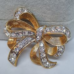 Vintage rhinestone ribbon brooch. Gold-tone textured metal with clear rhinestones brooch pin. Sparkly brooch for Christmas. Brooch size: 4x4.5 cm/1.6x1.7 inches. Mark- unsigned. Condition- excellent vintage. Maybe you want to see other brooches too: https://www.etsy.com/shop/VintageVoyageLT?ref=seller-platform-mcnav&section_id=32157229 You can write me a message if you have any questions. Glad you visited my store! Have a great time! Gold Crystal Brooch For Evening, Gold Crystal Brooches For Party, Gold Crystal Brooches With Bling, Gold Crystal Brooches For Formal Occasions, Glamorous Bling Brooches As A Gift, Glamorous Bling Brooches As Gift, Gold Rhinestone Pins For Party, Gold Rhinestone Party Pins, Gold Party Brooches With Bling