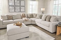 a living room with a large sectional couch and ottoman on the floor in front of two windows