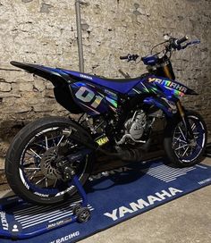 a blue motorcycle parked on top of a blue mat next to a stone wall with the words yamaha written on it