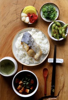 a plate with fish, rice and vegetables next to chopsticks on a wooden table