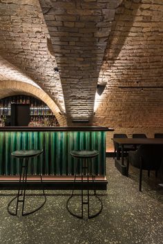 two stools are in front of a bar with green glass panels on the walls