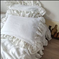 a pile of white ruffled pillows sitting on top of a wooden floor next to vases