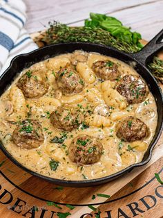 a skillet filled with pasta and meatballs on top of a wooden cutting board