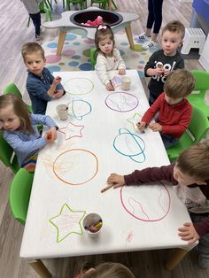 children are sitting at a table drawing with crayons on the paper and paint