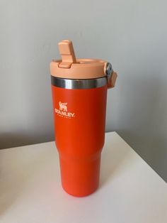 an orange insulated cup sitting on top of a white table next to a wall