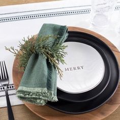 a place setting with black and white plates, napkins and silverware on a wooden table