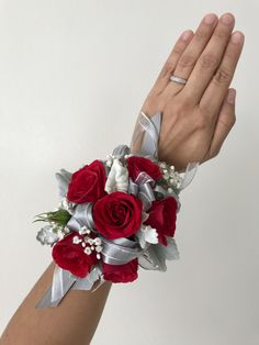 a woman's hand is holding a red rose wrist corsage with silver ribbon