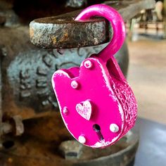 a pink heart shaped padlock is attached to a metal hook on a rusted piece of machinery