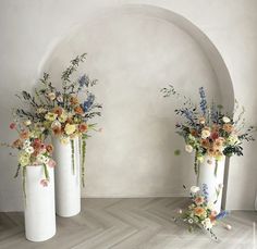 three white vases with flowers in them sitting on the floor next to each other