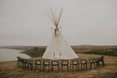 a teepee set up in the middle of a field with lots of chairs around it