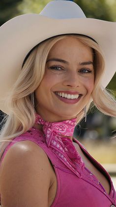 a woman with blonde hair wearing a pink shirt and cowboy hat smiling at the camera