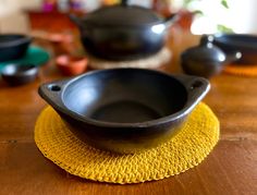 a wooden table topped with black bowls and saucers on top of a yellow place mat