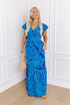 - Start your day on the sunny side with this beautiful maxi! With a timeless design and a chic floral print, this piece will keep you looking sweet around the clock. - Airy material with a blue hued botanical print - A built-in lining ending just above the hemline - A v-cut neckline - Short, flowy sleeves - A buttoned front that ends just above the hemline - A waistline with an elastic back - Functional side pockets - A relaxed silhouette that ends in a maxi length hemline that splits into an ac Spring Vacation Light Blue Maxi Dress, Light Blue Maxi Dress For Spring Vacation, Chic Light Blue Maxi Dress For Vacation, Blue Floral Print Floor-length Dress, Blue Floor-length Floral Print Dress, Blue Summer Maxi Dress For Vacation, Blue Summer Floor-length Maxi Dress, Summer Blue Floor-length Maxi Dress, Blue Floor-length Summer Maxi Dress