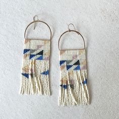 two small beaded earrings hanging from hooks on a white carpeted floor, one with blue and yellow beads