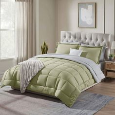 a bed with green comforter and pillows in a bedroom next to a large window