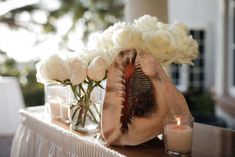 a vase filled with white roses next to a candle and some flowers on a table