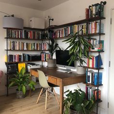 a home office with bookshelves full of books and plants on the desk area