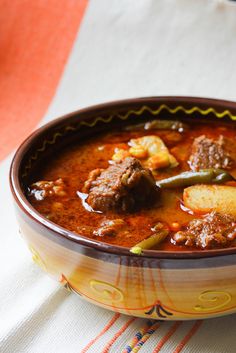 a bowl filled with meat and vegetables on top of a white table cloth next to a spoon