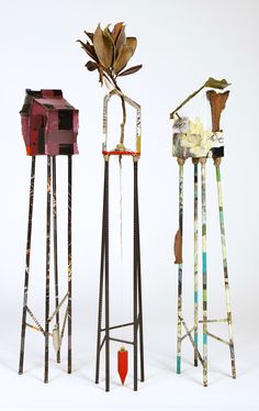 three tall metal sculptures with flowers in them on a white surface, one is red and the other is green