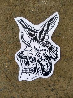 a sticker with a skull and two birds on it's head is sitting on the ground