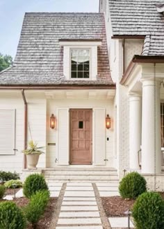 a white house with steps leading up to the front door and entry way that is surrounded by bushes