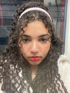 a young woman with curly hair wearing a white headband and looking at the camera