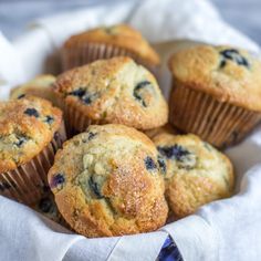 blueberry muffins in a white basket on a tablecloth with a striped napkin