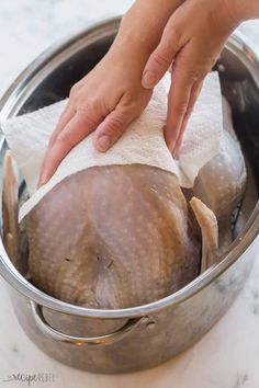 a person wiping the top of a turkey in a pot with a cloth on it