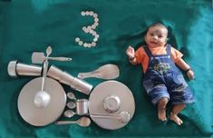 a baby laying on top of a green blanket next to utensils and spoons