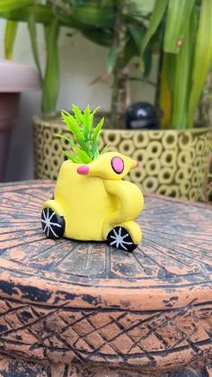 a yellow toy car with a plant in the back