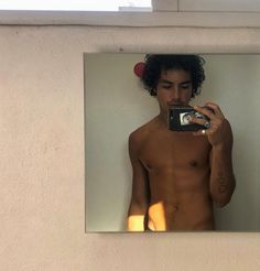 a shirtless man taking a selfie in front of a mirror with his cell phone