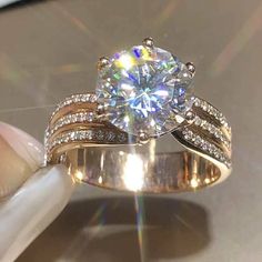 a woman's hand holding an engagement ring on top of a white and gold plated surface