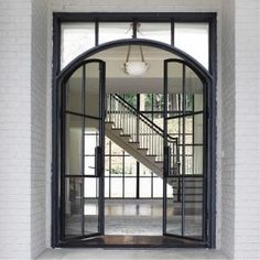 an open door leading to a stairway in a white brick building with arched glass doors